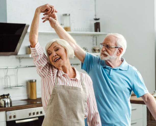 Seniori-ikäinen pariskunta tanssii keittiössään.